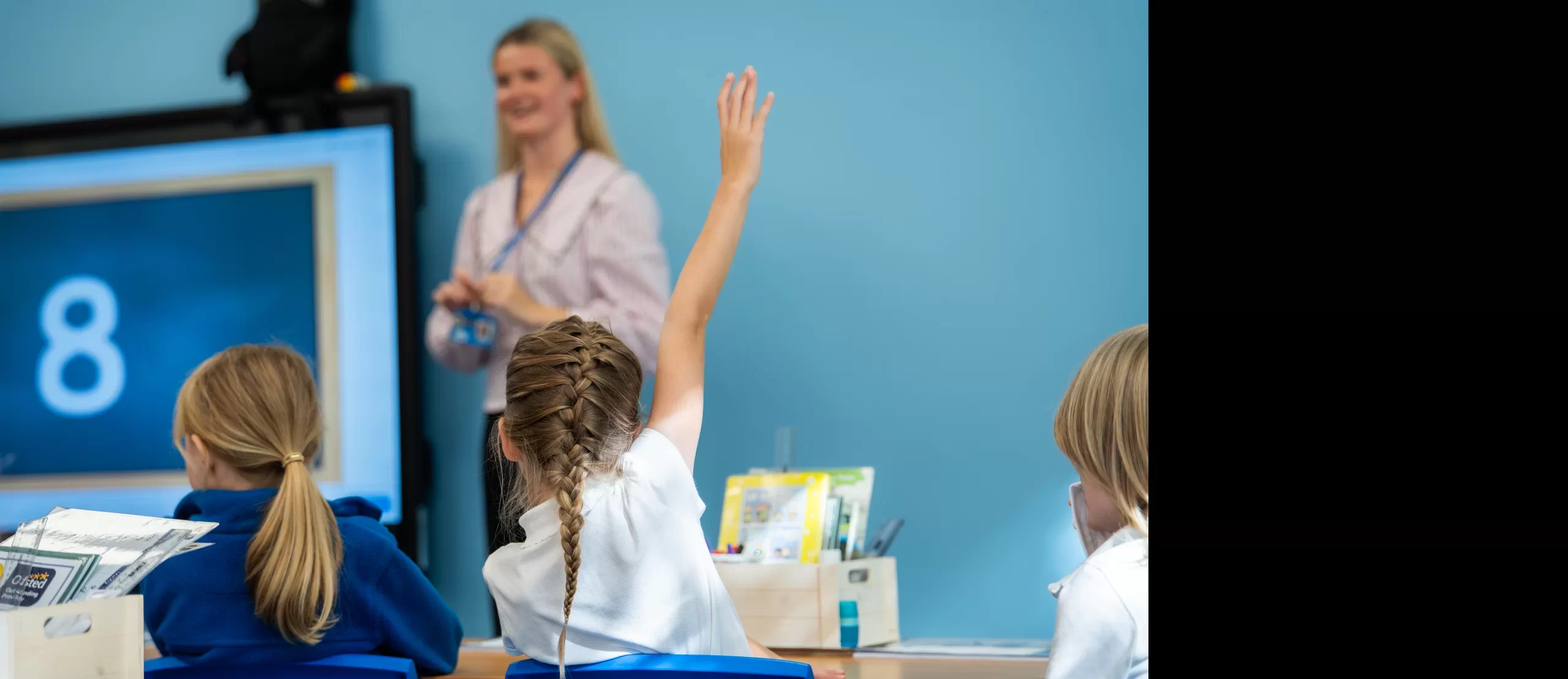 a kid raising its arm in a class room setting with the teacher in the front
